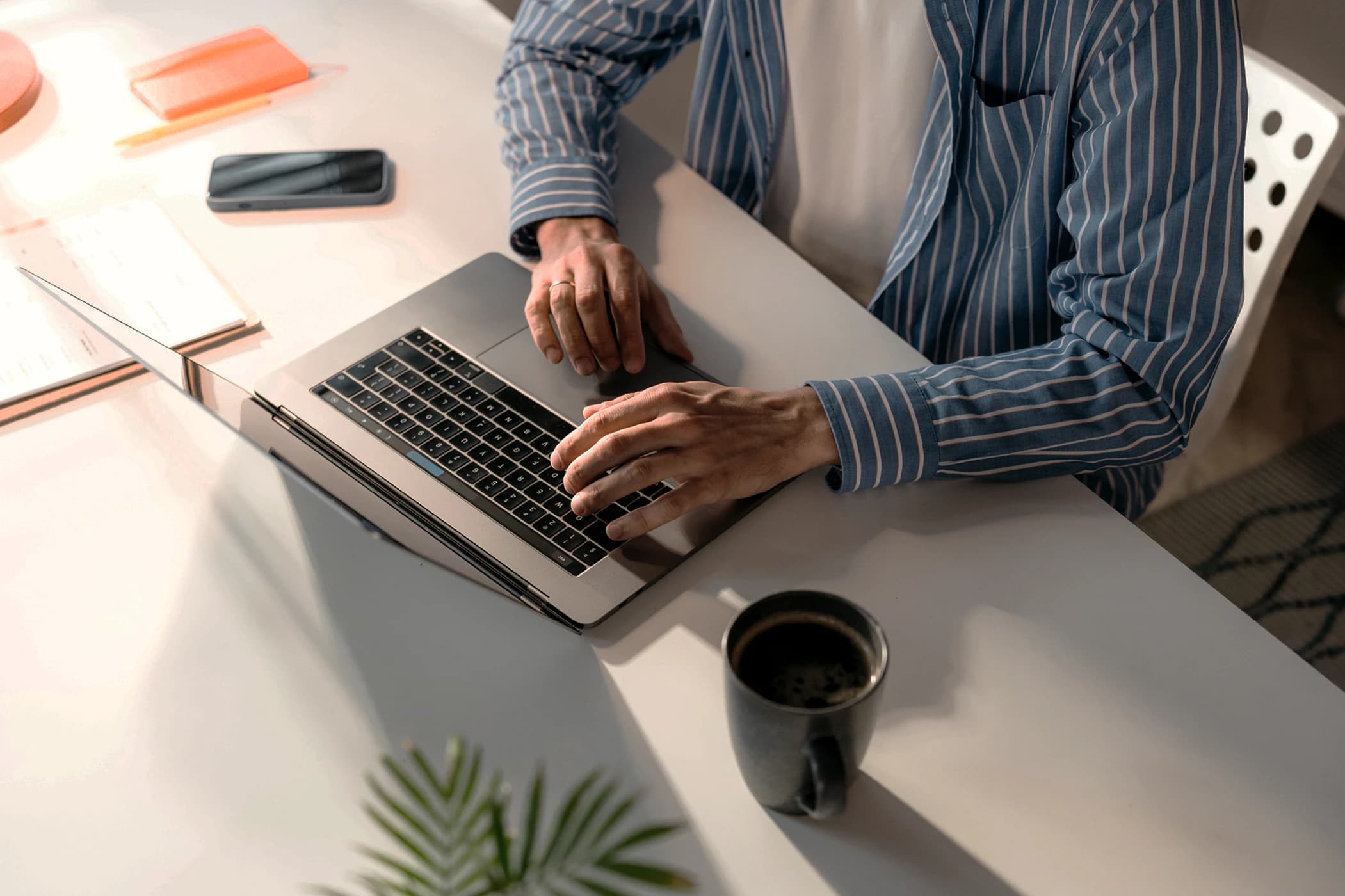 Hands typing on a laptop at a desk next to a cup of coffee.